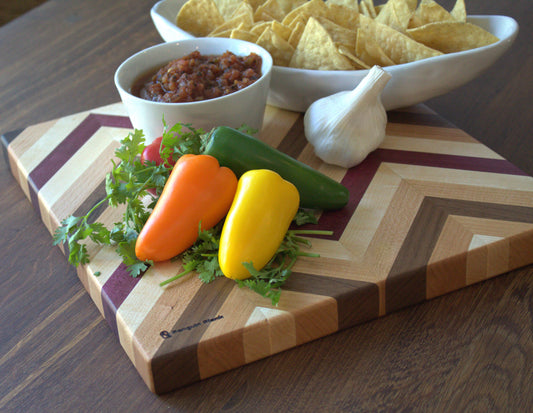 Herringbone cutting board with chips, salsa, peppers and garlic.