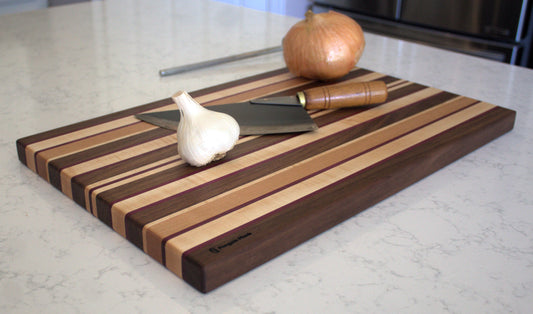 Large Wood Cutting Board, made from a unique blend of Walnut, Maple, Cherry, and Purpleheart, shown with knife garlic and onion.